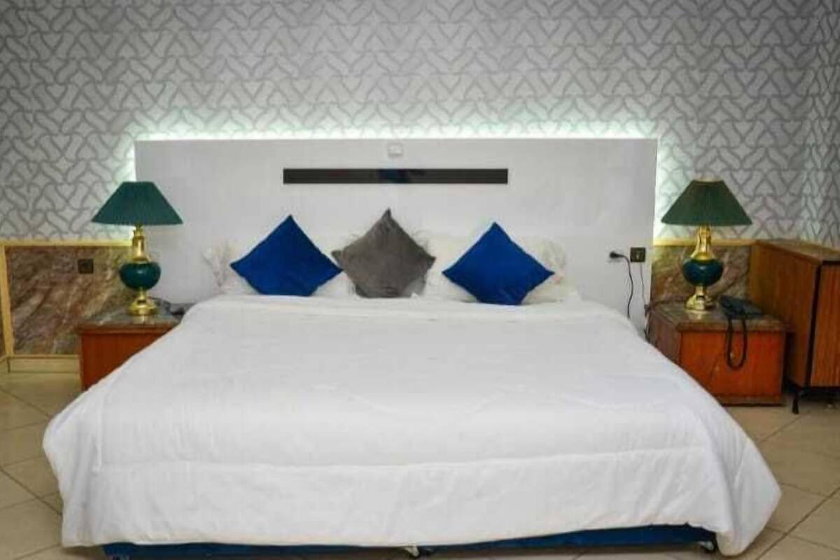 A neatly made bed with a white comforter and blue and gray pillows, flanked by two nightstands with lamps.