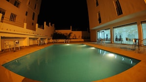 Una piscina con borde de baldosas, rodeada de edificios con ventanas amplias y zonas de estar al aire libre.