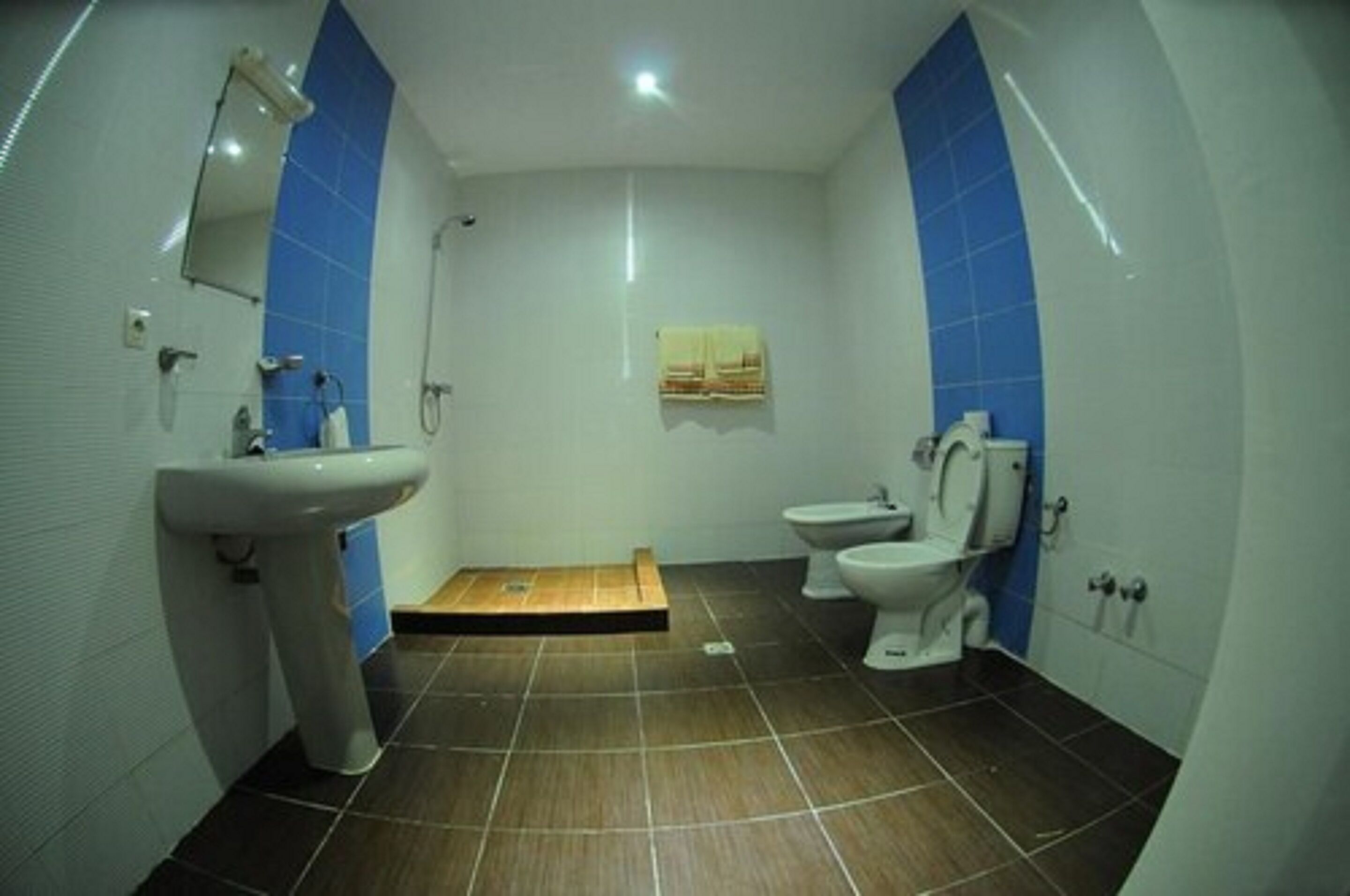 Une salle de bain comprenant un lavabo, des toilettes et un bidet, avec un carrelage au sol et des murs d’accent bleu.