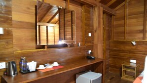 A wooden cabin interior with a wooden counter, a small refrigerator, a mirror, and a wooden stool.