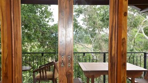 A wooden deck with a table and chairs, surrounded by a black railing, overlooking a lush green landscape.