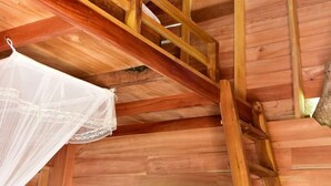 A wooden interior with a staircase, a bed with a white canopy, and a wooden door.
