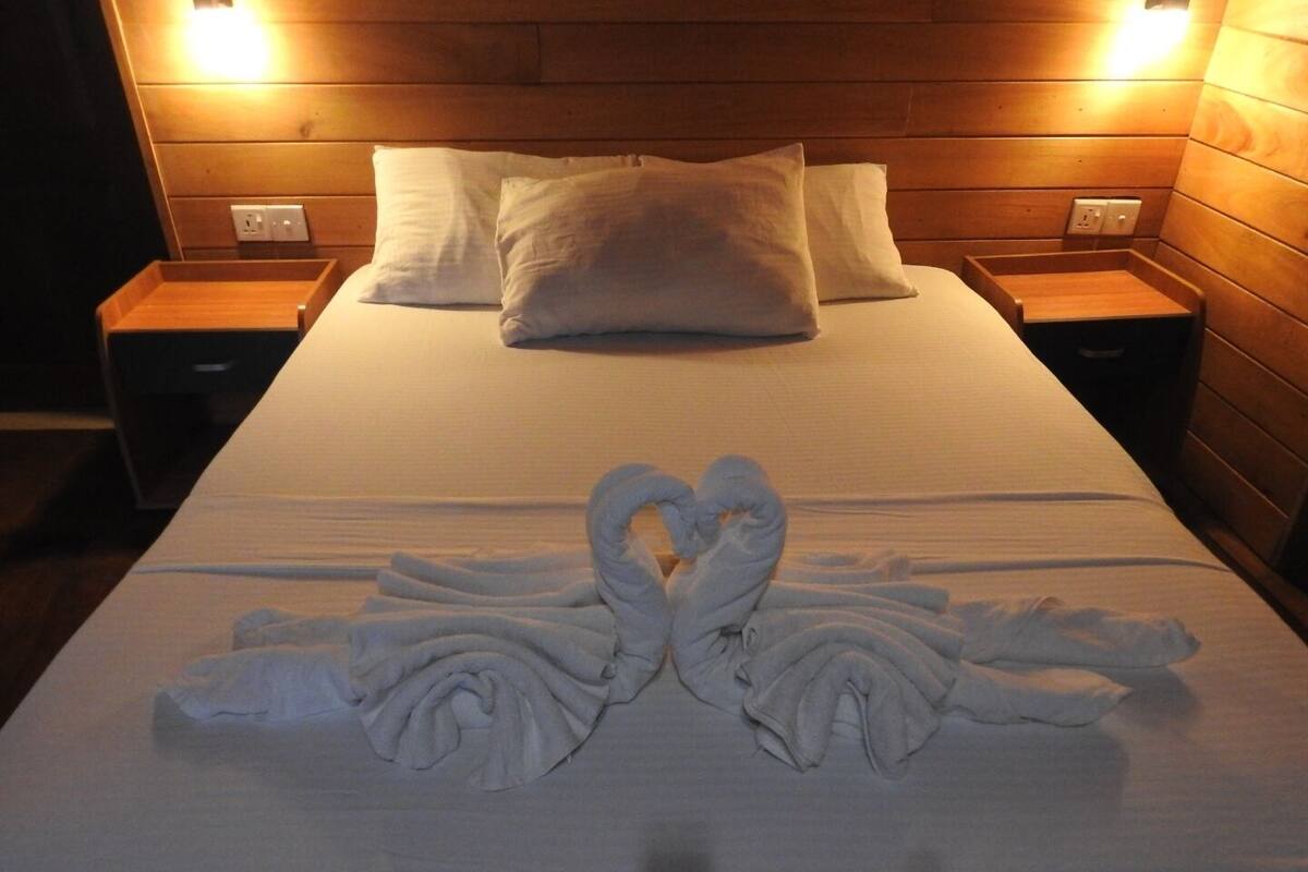 Ein Hotelzimmer mit einem hölzernen Kopfteil, zwei Nachttischen und einem Bett mit weißer Bettdecke und Kissen.