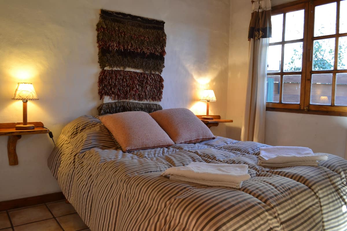 Una cama bien tendida con ropa de cama a rayas, dos lámparas de noche y un tapiz en la pared.