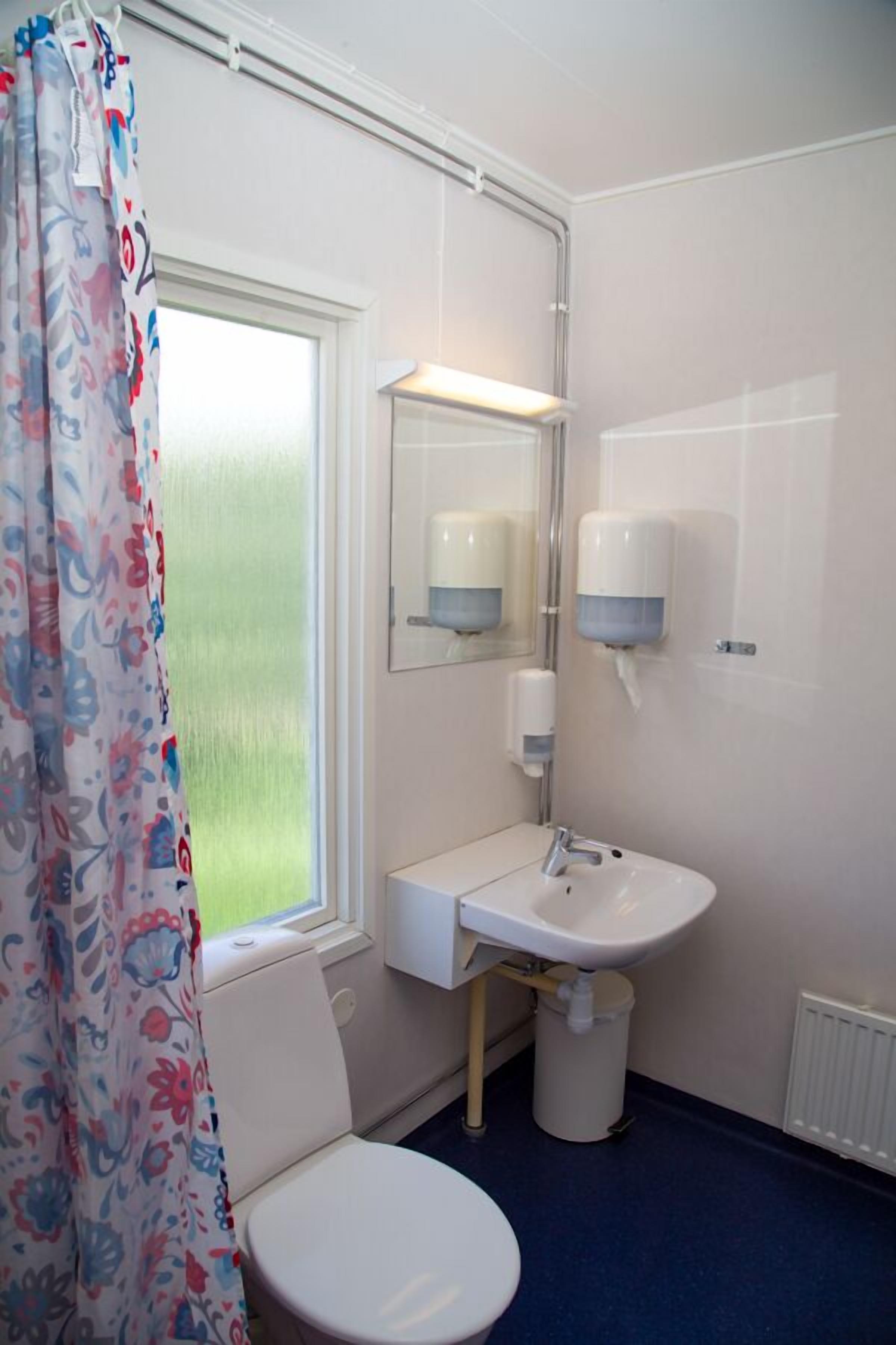 Ein Badezimmer mit Toilette, Waschbecken, Spiegel und einem Fenster mit Vorhängen.