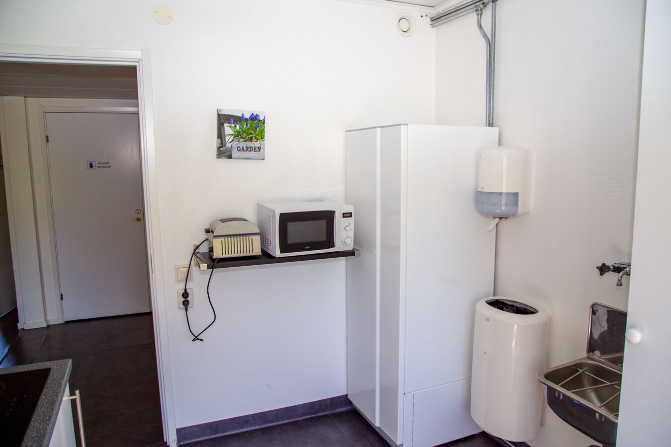 Een compact keukenhoekje met een magnetron, een klein prullenbakje en een waterdispenser.