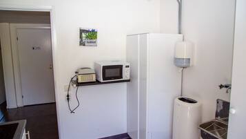 Een compact keukenhoekje met een magnetron, een klein prullenbakje en een waterdispenser.