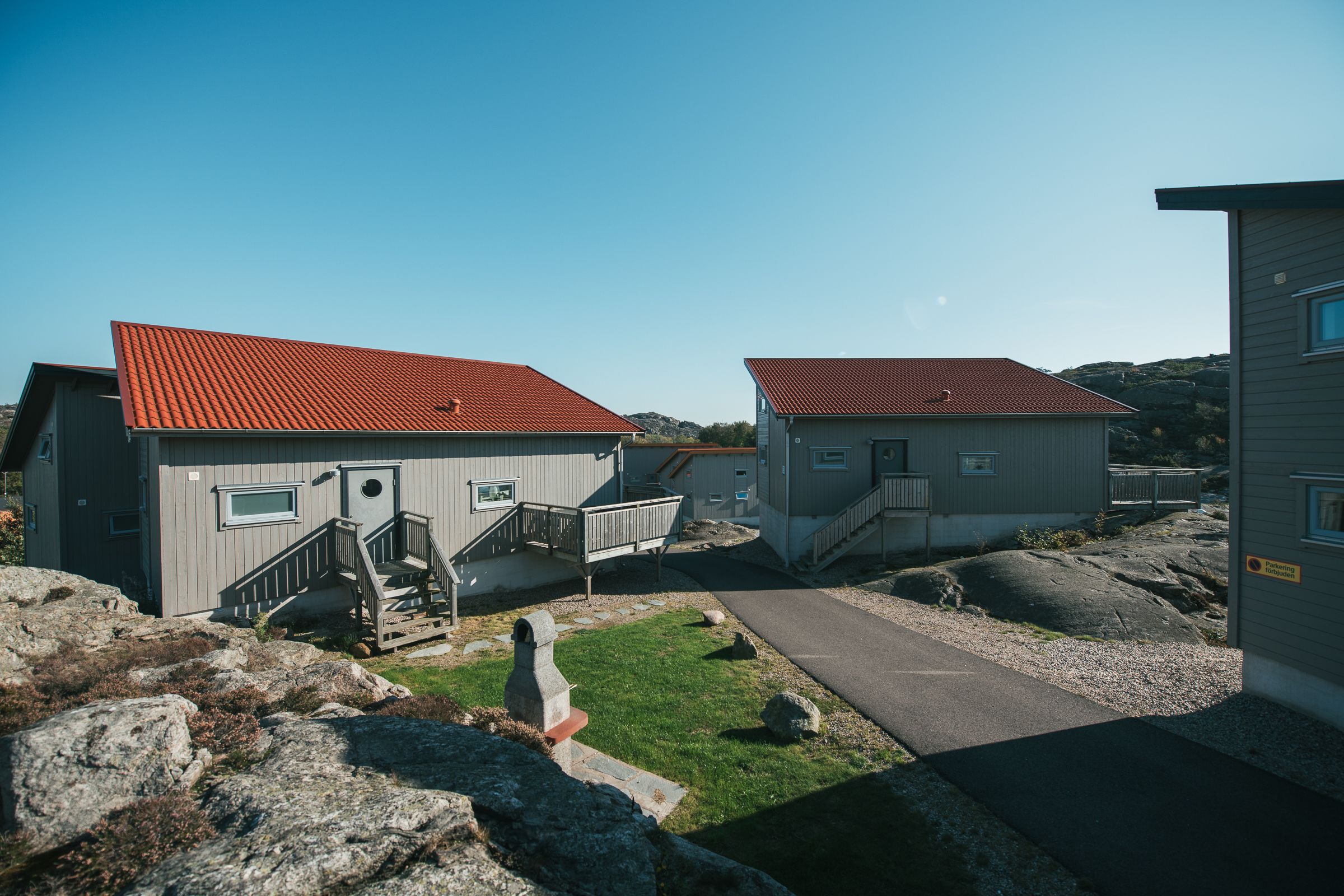 A row of two-story buildings with red-tiled roofs, a central pathway, and a rocky landscape.