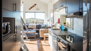 A modern kitchen with a built-in oven, a dining area with a sofa and table, and a view of the outdoors. - Hav & Logi Skärhamn (Skaerhamn)