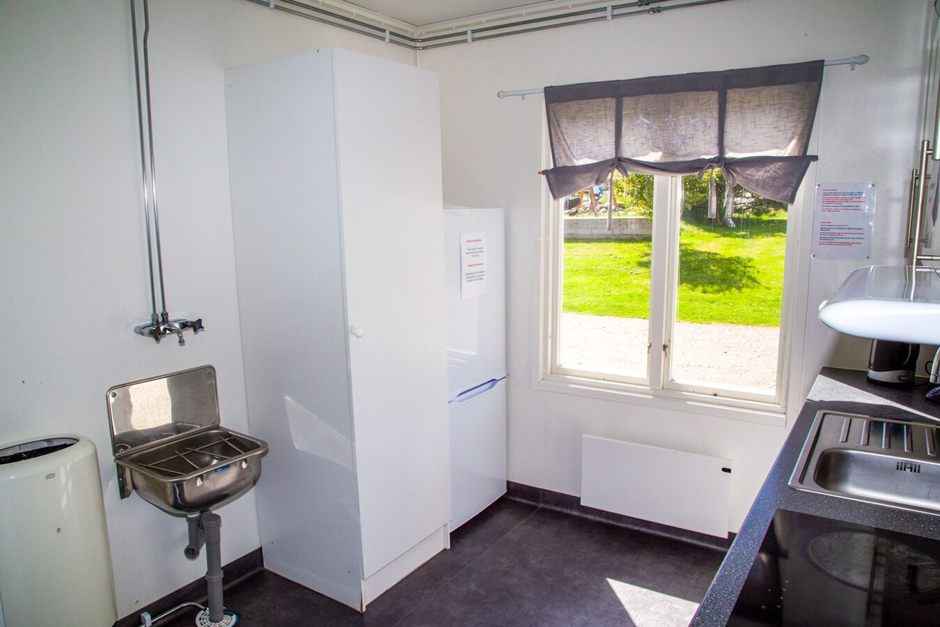 Een compacte keuken met een spoelbak, een raam met gordijnen, een koelkast en een klein aanrecht.