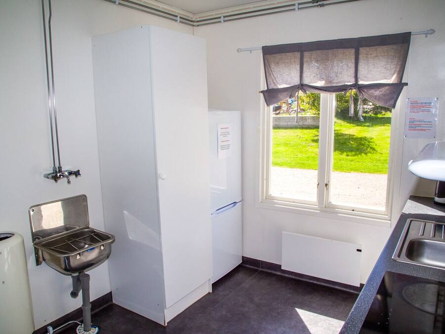 A compact kitchen with a sink, a window with curtains, a refrigerator, and a small countertop.