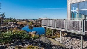 A modern building with a wooden deck overlooking a rocky shoreline and a calm body of water. - Hav & Logi Skärhamn (Skaerhamn)