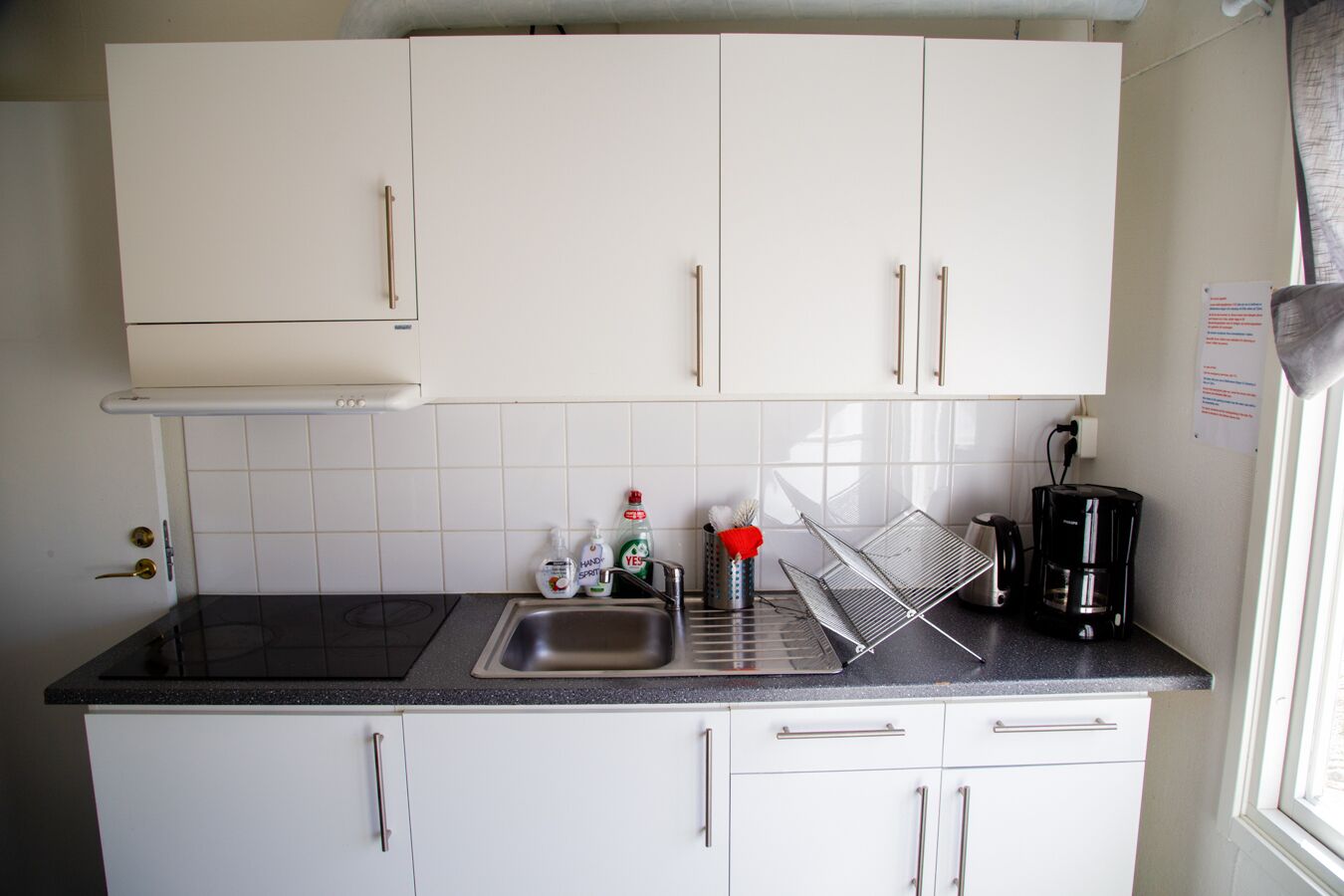 Een kleine keuken met witte kastjes, een zwart aanrecht, een roestvrijstalen spoelbak en een koffiezetapparaat.