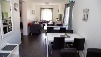Ett modernt hotellrum med en matplats, en soffgrupp, ett litet kök och ett stort fönster med gardiner.