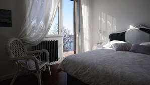 Una camera da letto con un letto grande, una sedia, un termosifone e una finestra con tende leggere.