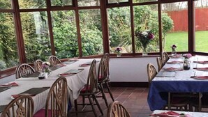 A dining area with tables set for four, wooden chairs, and large windows offering a view of a garden. - The Halfway House Inn (Bridgnorth)