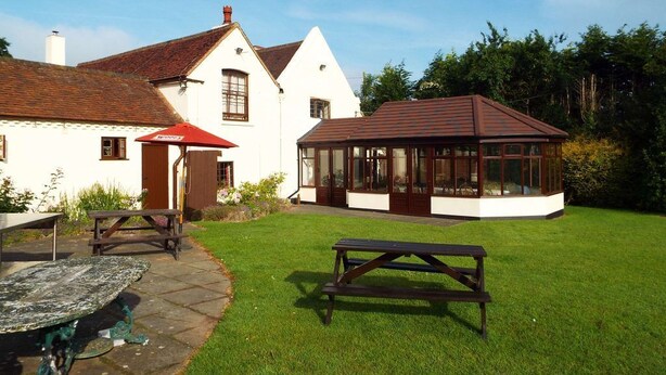 A white building with a red roof, a glass conservatory, and a picnic table in a grassy area. - The Halfway House Inn (Bridgnorth)