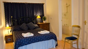 A bedroom with a bed, bedside tables, a chair, a lamp, a potted plant, and a bathroom with a shower and bathtub. - The Halfway House Inn (Bridgnorth)