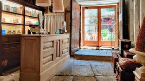 Un interior rústico con una barra de madera, un ventanal con vistas a la vegetación y objetos antiguos en estantes.