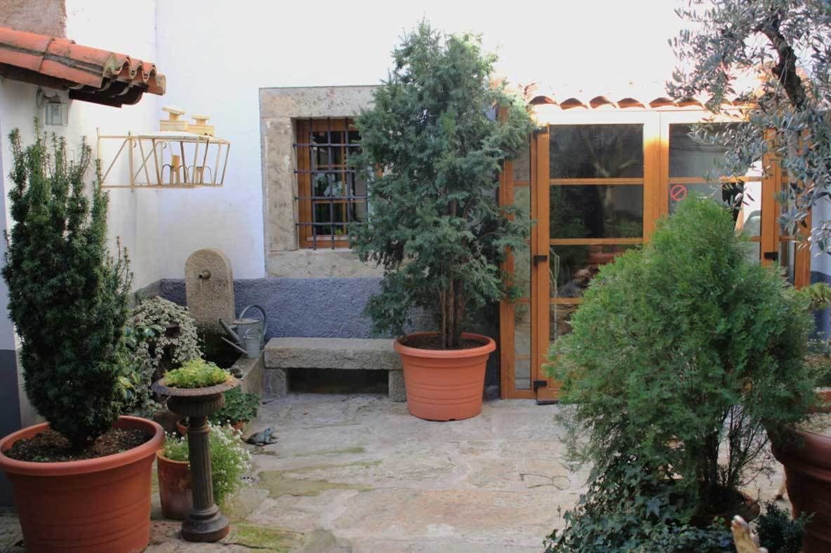 Une cour avec des plantes en pot, un banc en pierre et une porte en bois.