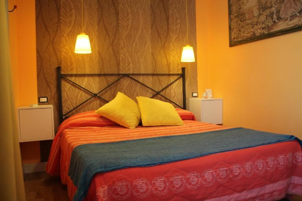 A hotel room with a bed, two bedside lamps, a nightstand, and a wall with a patterned wallpaper.