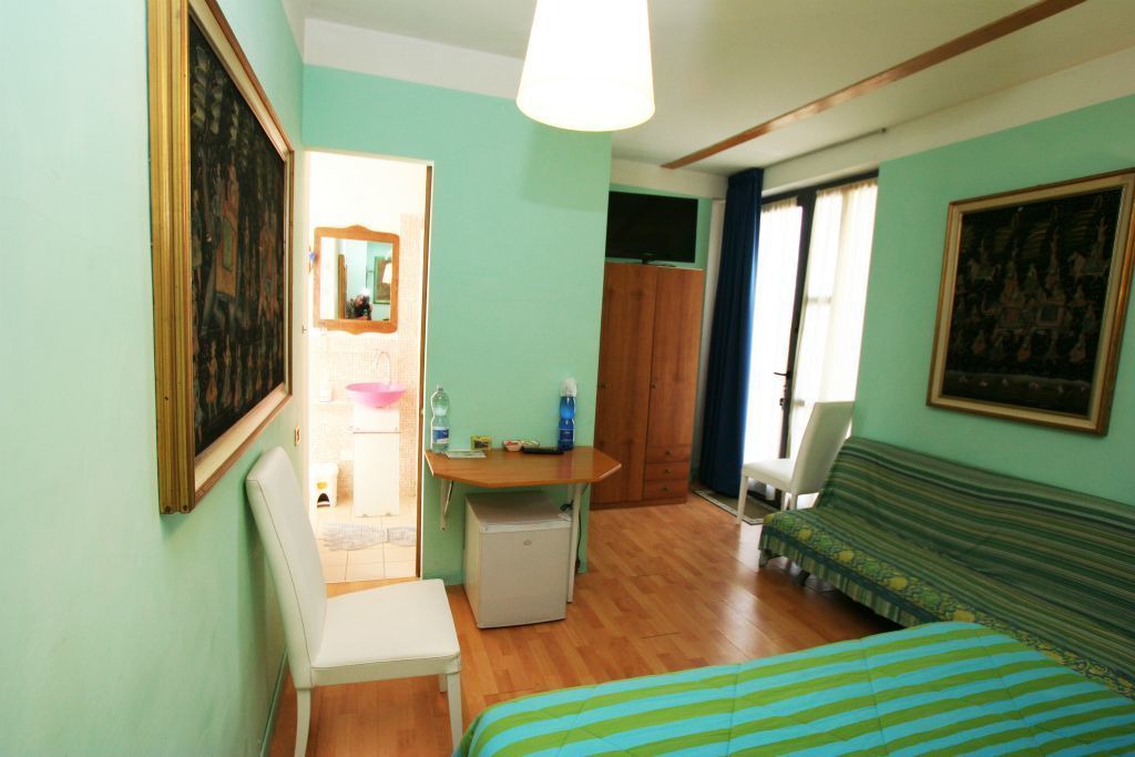 Une petite pièce bien éclairée, équipée d’un lit, d’un bureau, d’une chaise et d’un réfrigérateur.