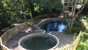 Une terrasse en bois entoure une fontaine circulaire, elle-même bordée d’une rambarde en bois.