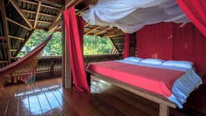 Une chambre avec un lit, un hamac et une vue sur la verdure.