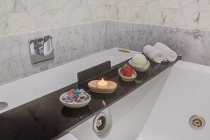 A bathroom with a marble wall, a black countertop, a candle, a bowl of colorful bath salts, a bowl of strawberries, and rolled towels. - Transamerica Collection Goiânia (Goiania)