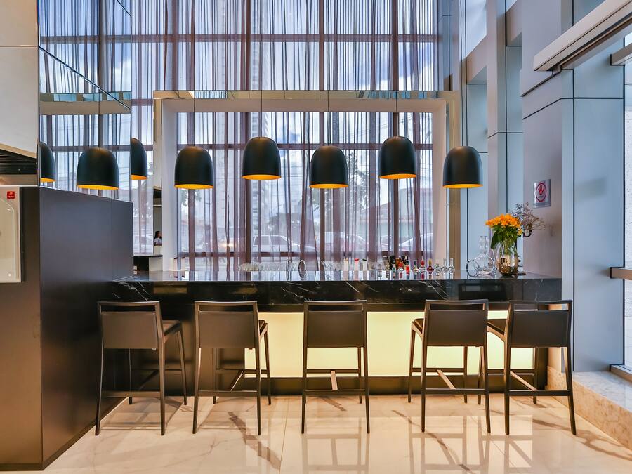 Zona de bar moderna con una encimera negra, cinco taburetes y lámparas colgantes negras.