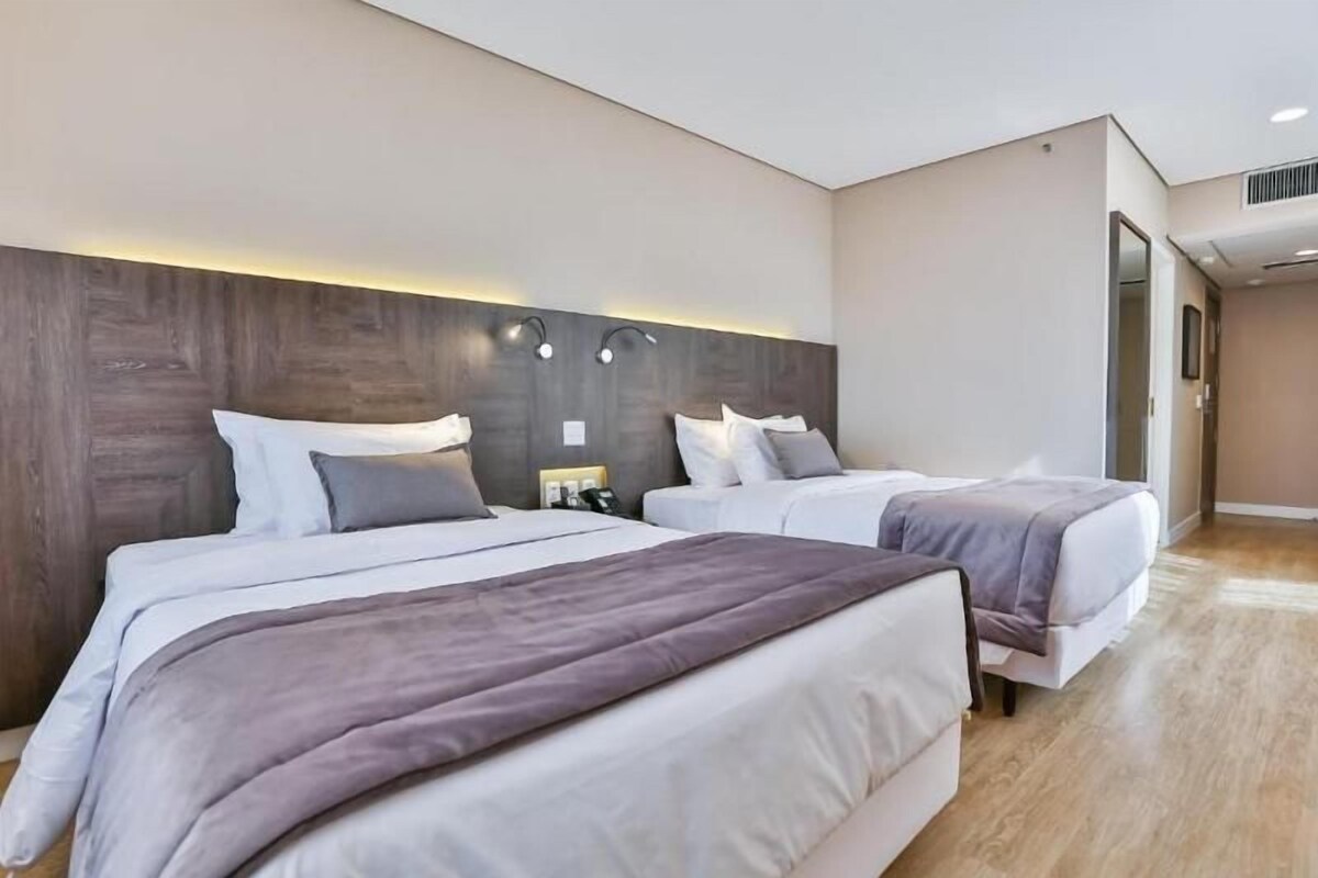 A hotel room with two beds, a wooden headboard, bedside lamps, and a wooden floor.