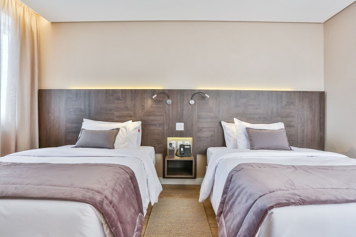 Habitació d'hotel amb dos llits, una taula de nit amb una làmpada i una petita estant amb un telèfon.
