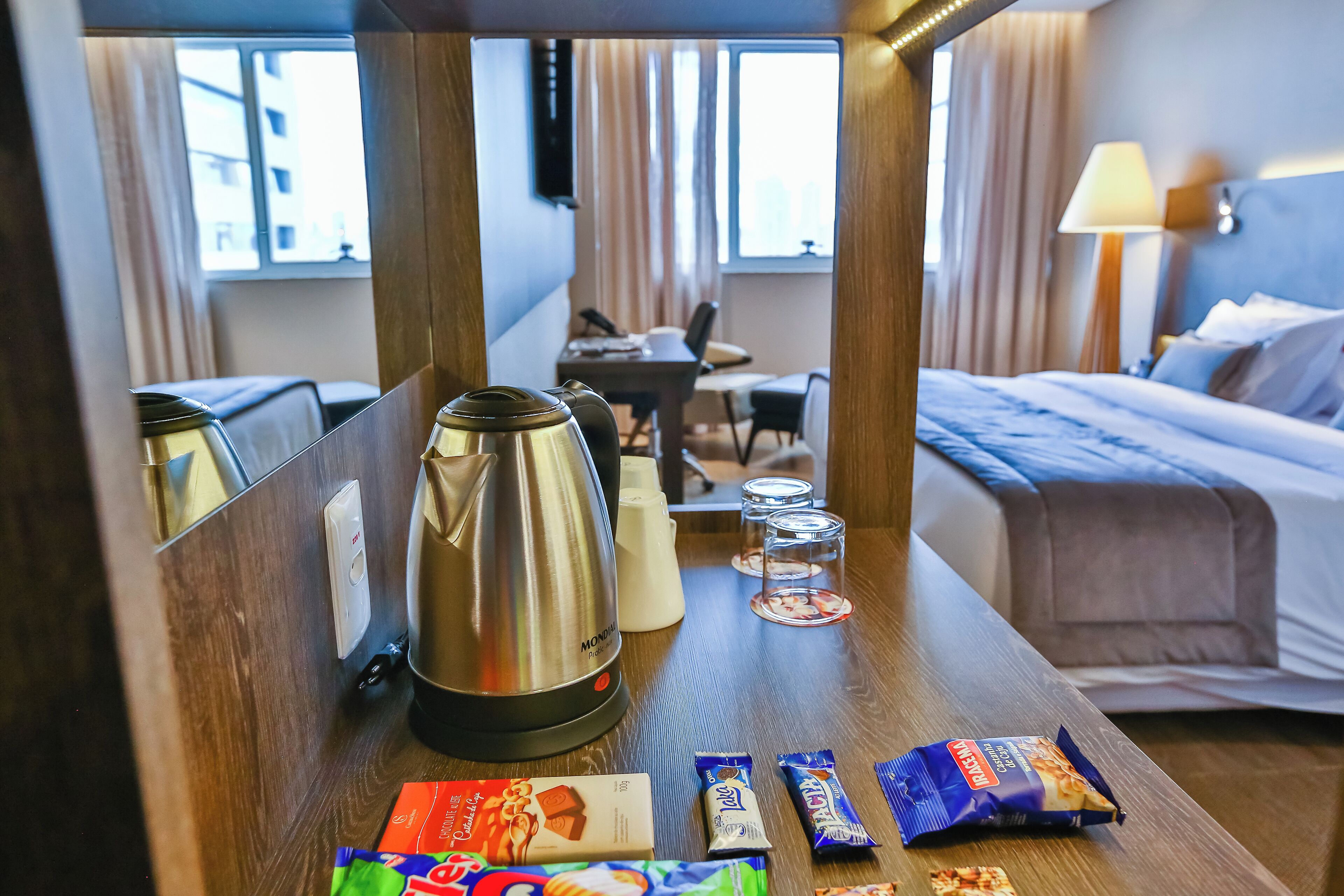 Une chambre d’hôtel avec un lit, un bureau, une machine à café et quelques collations sur la table.