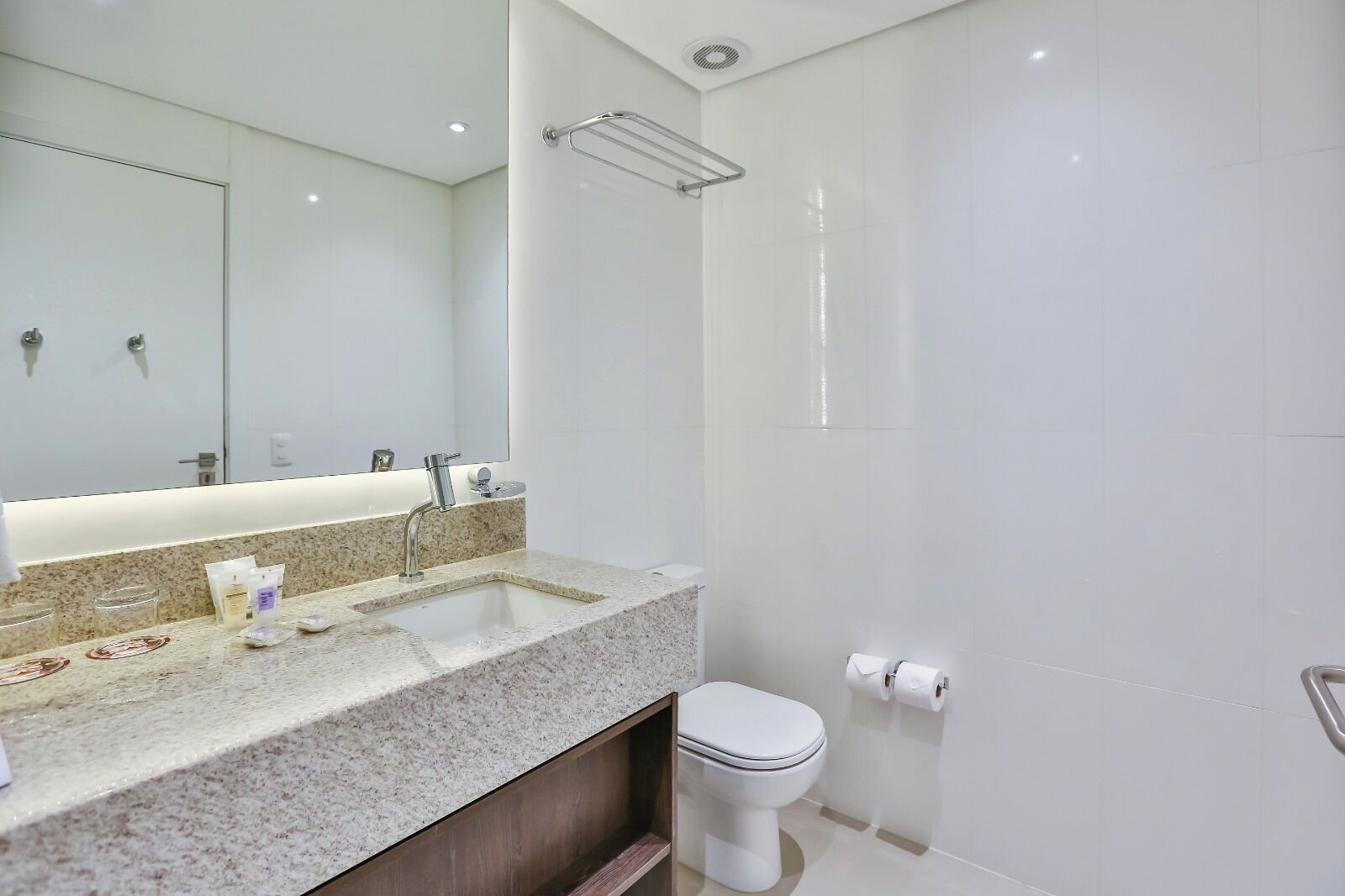 A modern bathroom with a granite countertop, a white sink, a mirror, a toilet, and a shower area.