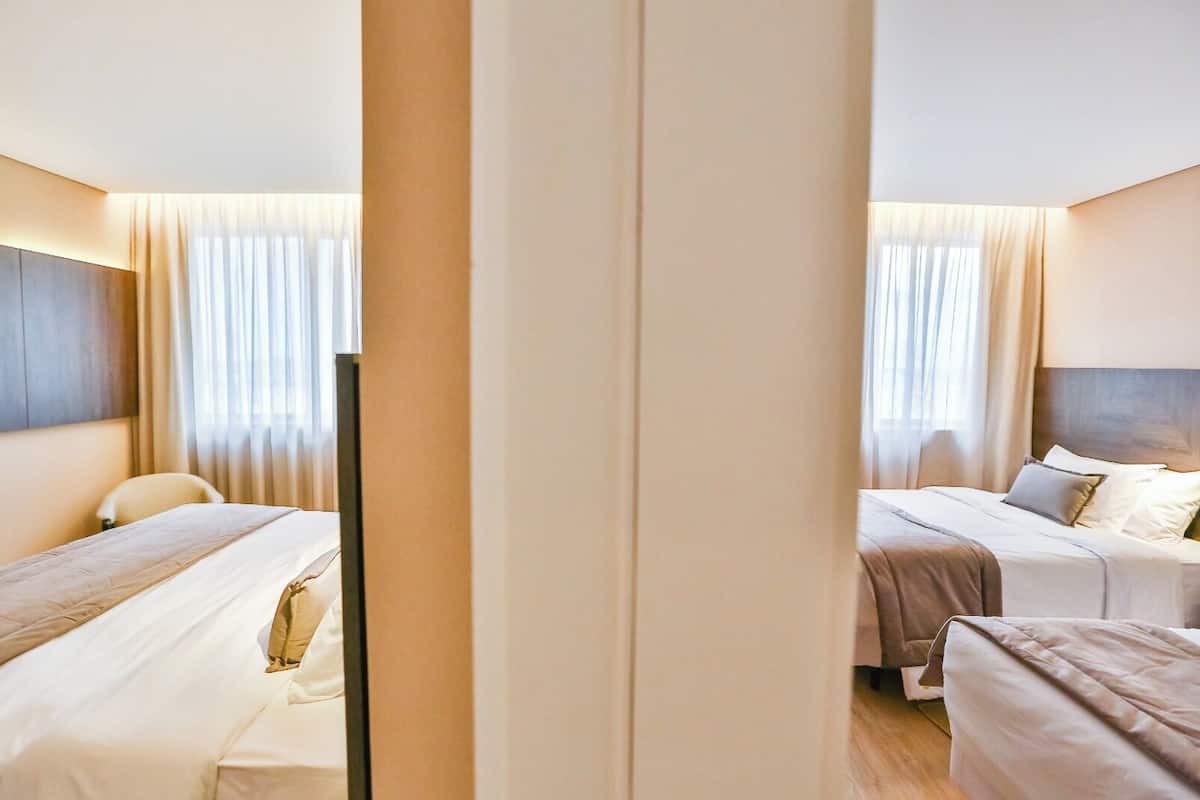 Una camera d'albergo con due letti, una scrivania e un'ampia finestra con tende.