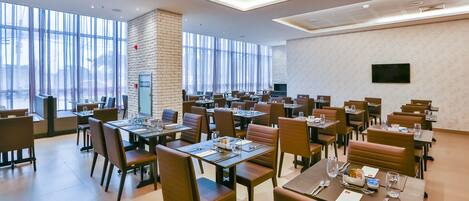 A spacious dining area with multiple tables and chairs, large windows, and a modern ceiling design.