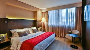 Habitación de hotel con una cama grande, una mesita de noche con teléfono, una lámpara y una silla junto a la ventana.