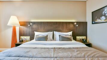 Habitación de hotel con una cama grande, cabecera de madera, mesitas de noche con lámparas y teléfono en la pared.