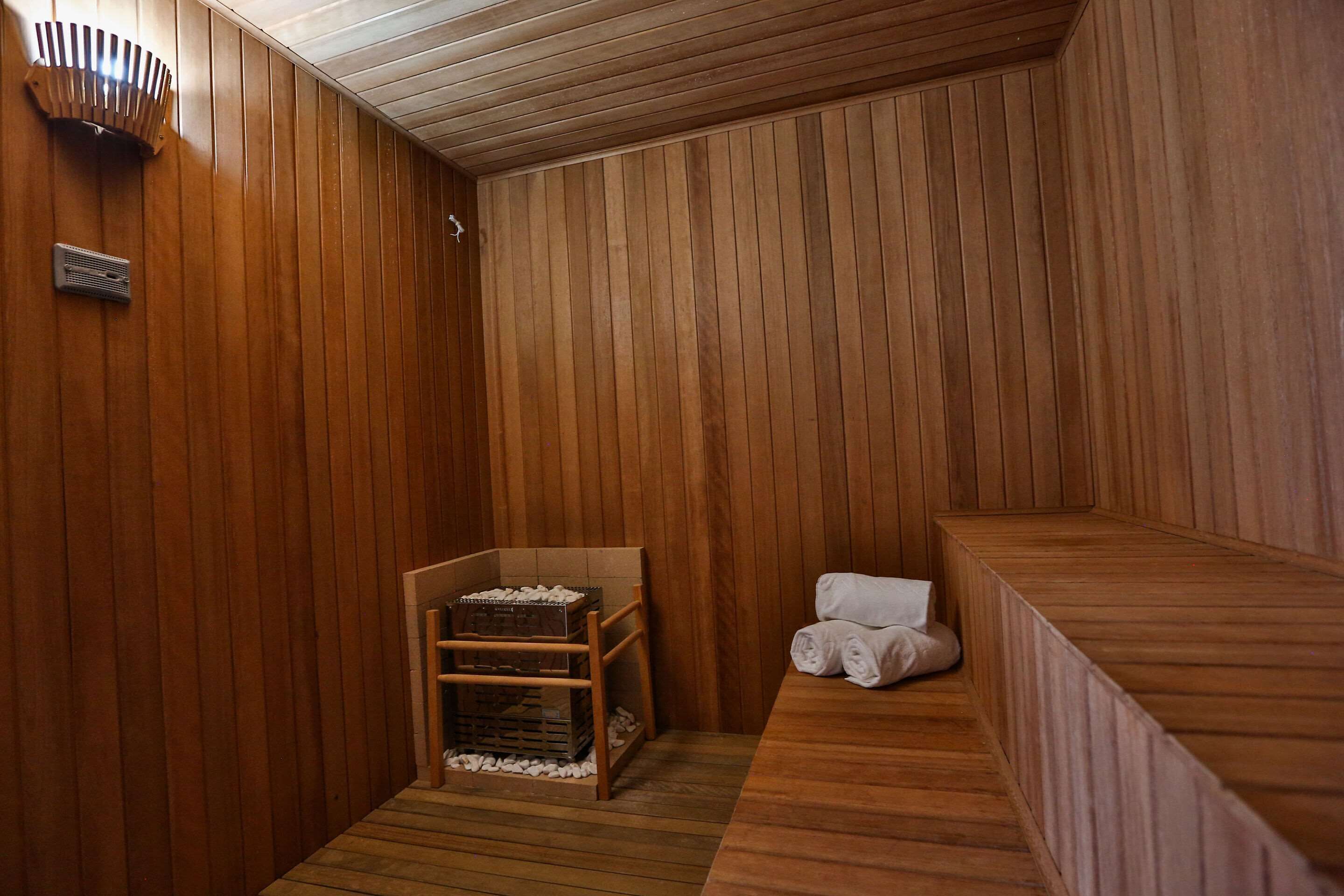 A wooden sauna with a bench, a small seating area, and a wooden shelf with items.