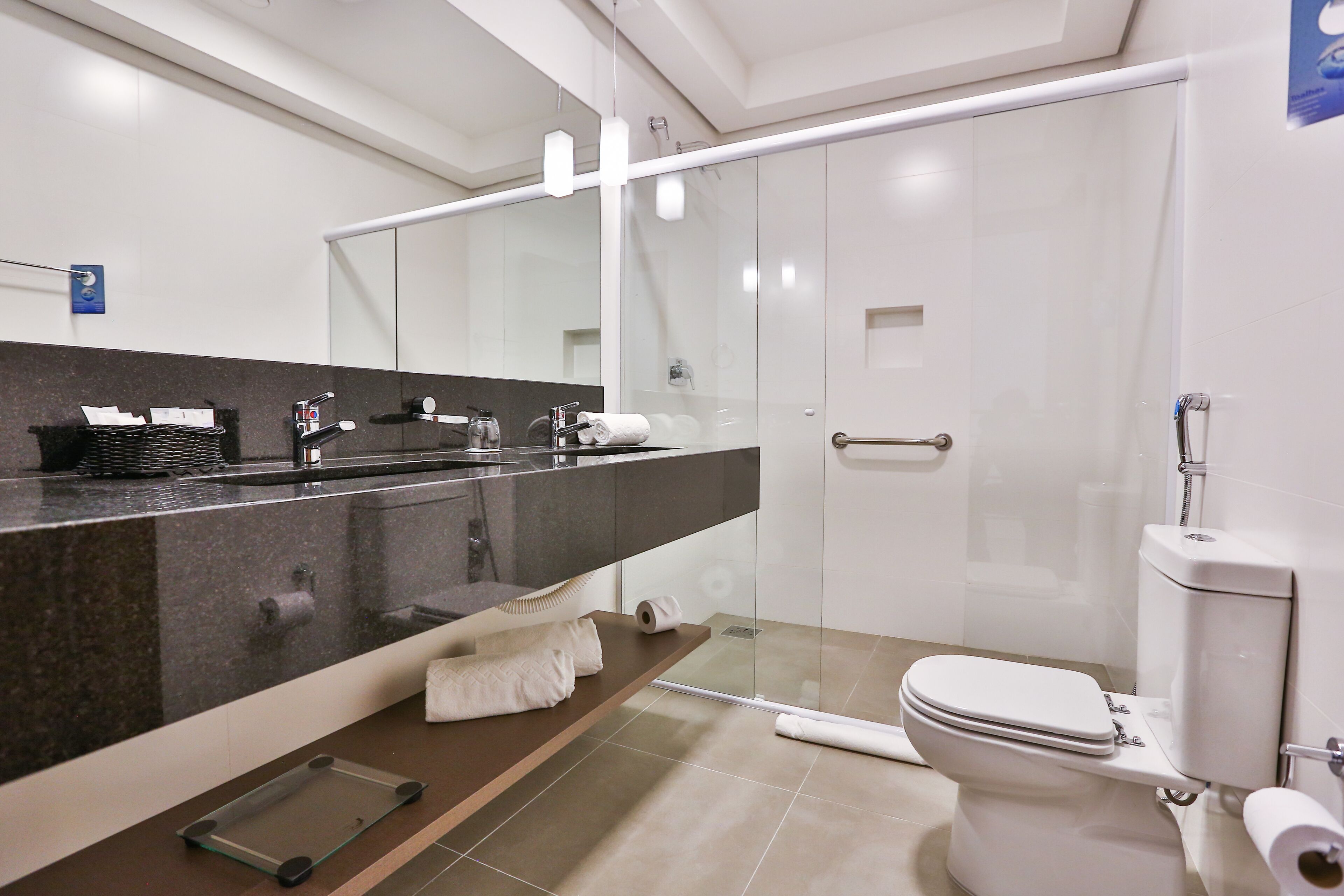A modern bathroom with a large mirror, a glass shower enclosure, a toilet, and a sink with a towel rack.