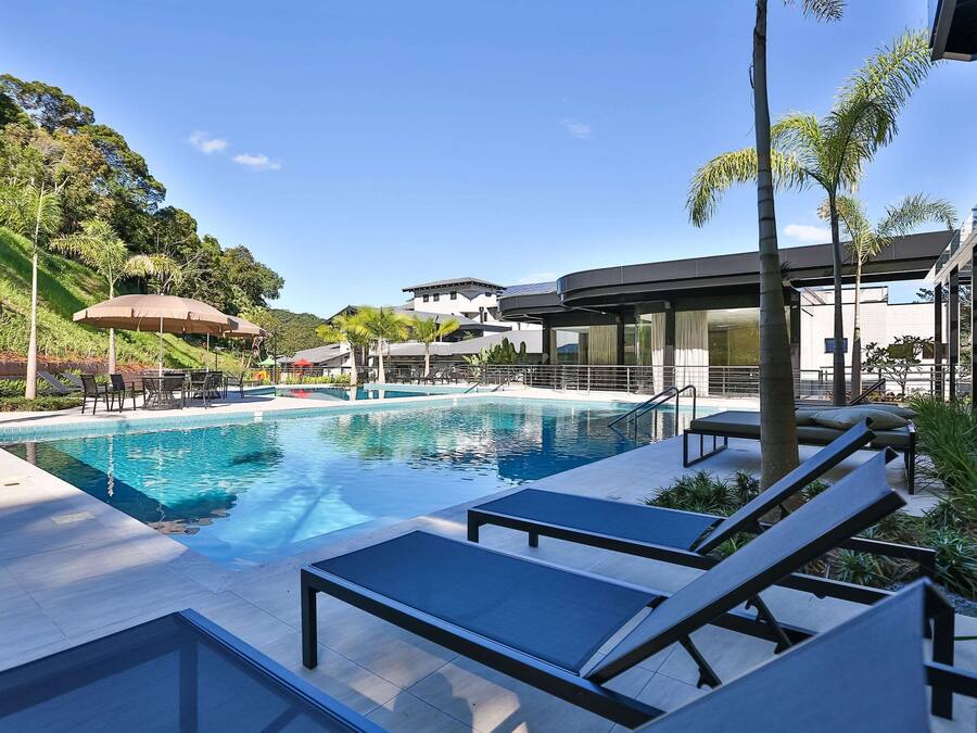 A swimming pool with lounge chairs and umbrellas, surrounded by greenery and modern buildings.