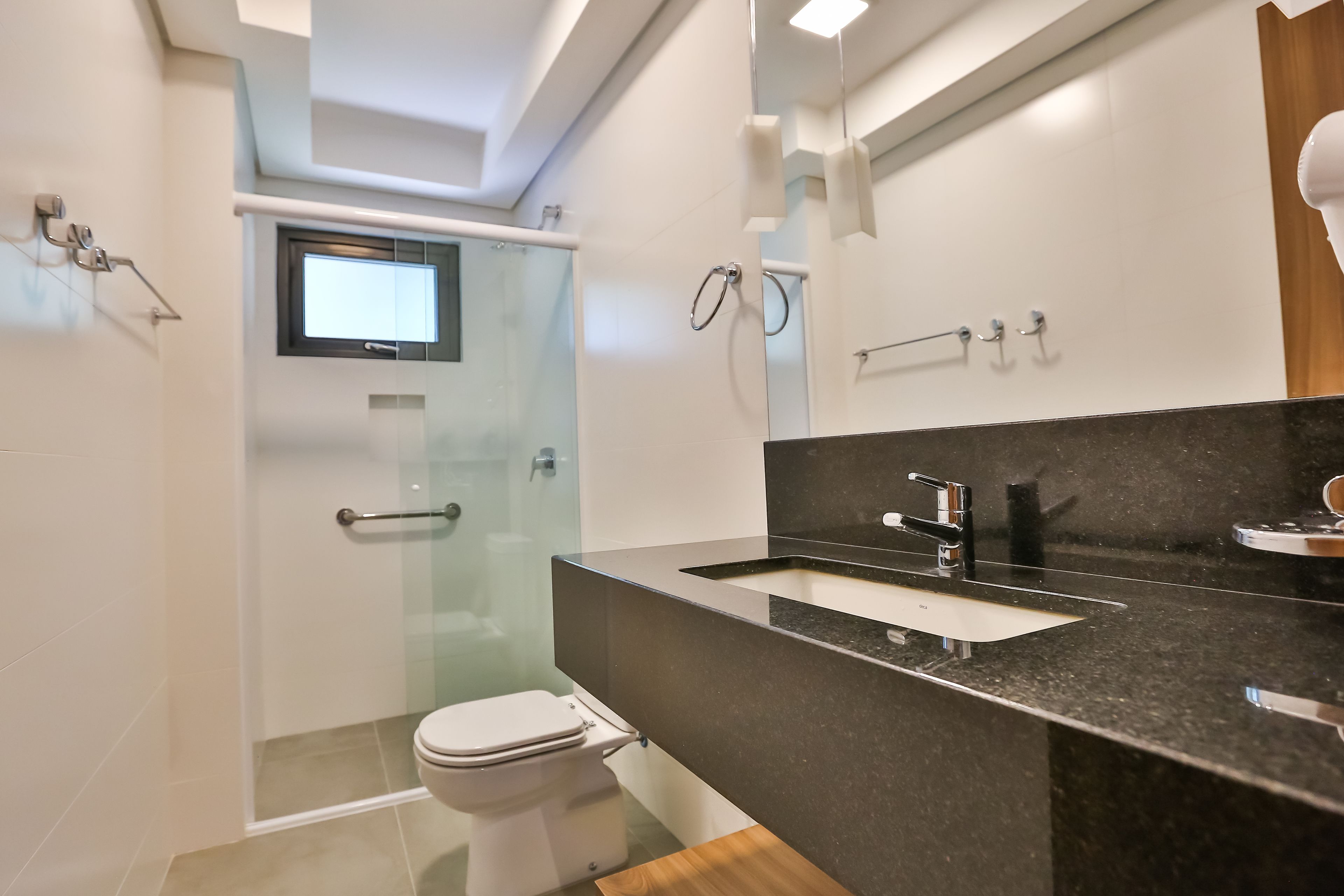A modern bathroom with a glass shower enclosure, a white toilet, a black countertop sink, and a mirror.