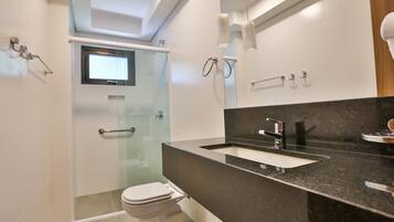Un baño moderno con cabina de ducha de vidrio, inodoro blanco, lavamanos con encimera negra y un espejo.