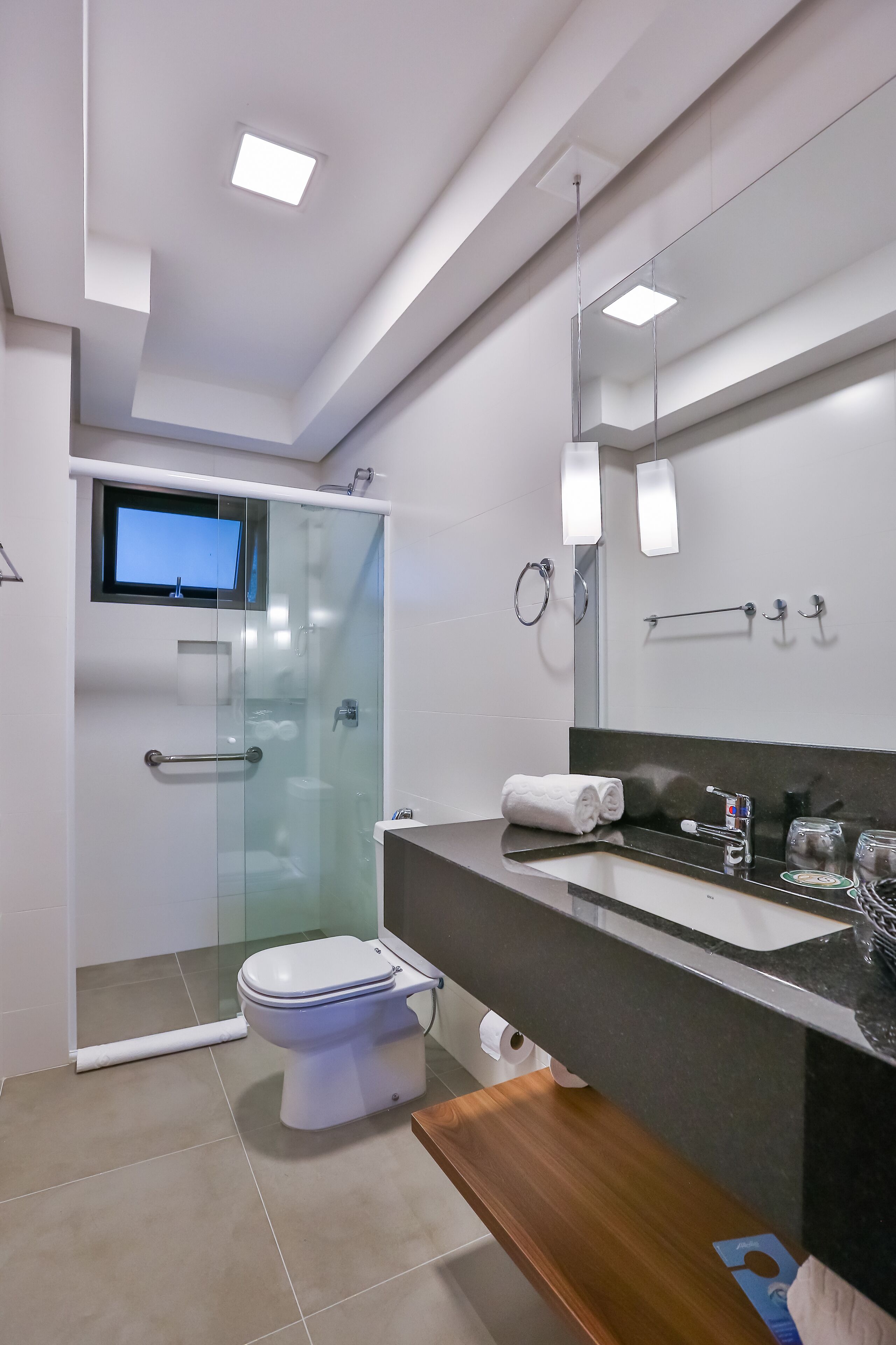 Un baño moderno con ducha de vidrio, inodoro, tocador con espejo y televisor montado en la pared.