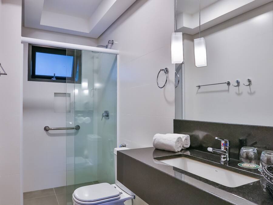 Un baño moderno con ducha de vidrio, inodoro, tocador con espejo y televisor montado en la pared.