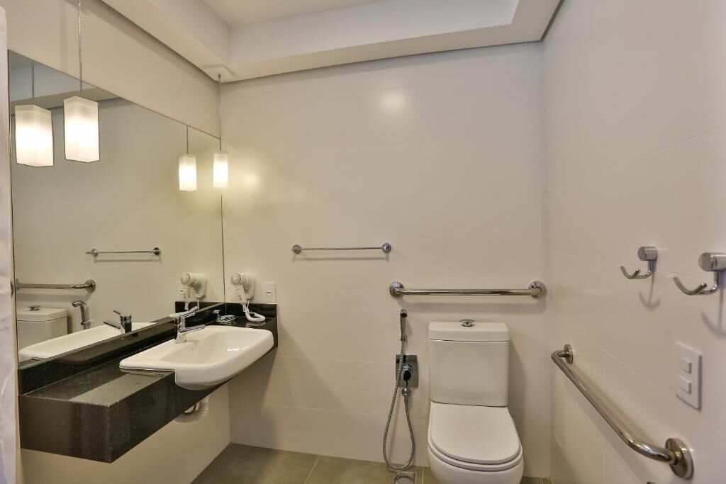 A modern bathroom with a white sink, mirror, and toilet. It includes grab bars and a shower area.