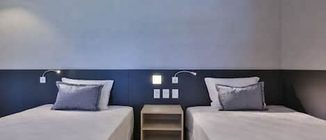 Habitación de hotel con dos camas, una estantería empotrada e iluminación en la pared.