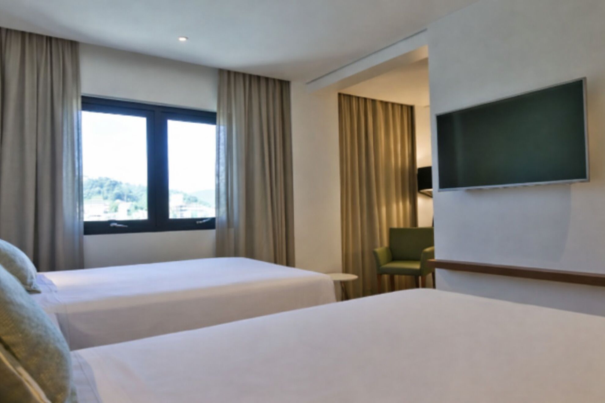 Habitación de hotel con dos camas, un televisor, una silla y un ventanal con cortinas.