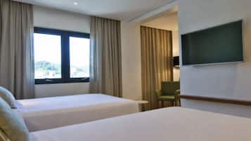 Habitación de hotel con dos camas, un televisor, una silla y un ventanal con cortinas.