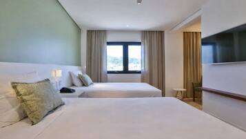 Habitación de hotel con dos camas, televisión, ventana con cortinas y una mesita.